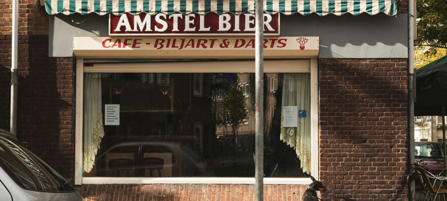 Traditioneel café in Amsterdam met Amstel Bier-bord, biljart & darts en een hond voor de gevel